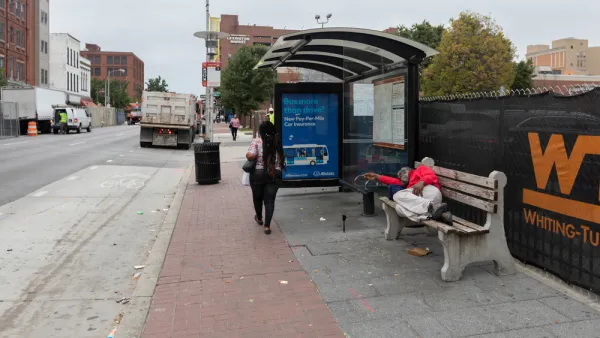 Unhoused person sleeping on bench at bus stop on Baltimore street