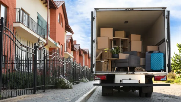 View of back of moving van with back door open, loaded with boxes, next to a line of two-story apartment buildings.