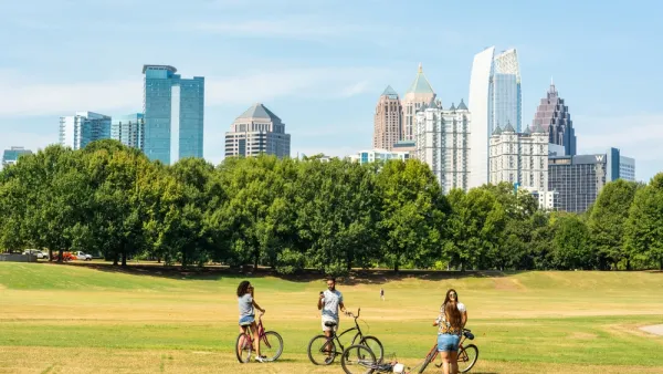 Three people with bikes stopping to chat on grassy field with Atlanta, Georgia skyline in background