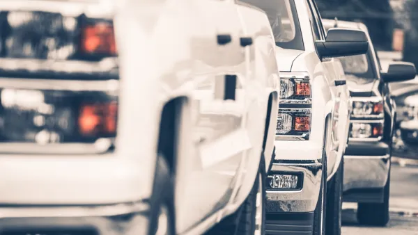 Close-up of white pick-up truck on sales lot from front driver's side; two more trucks behind it