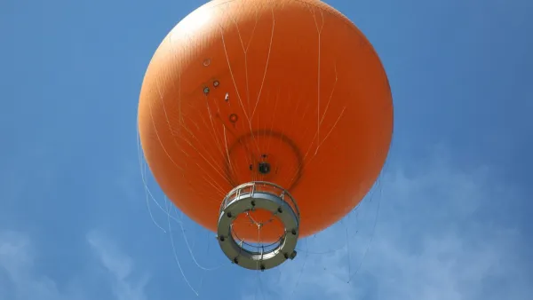View from below of orange tethered hot-air balloon floating in blue sky