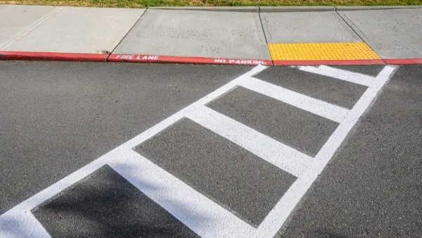 Freshly painted white crosswalk leading to yellow curb cut to sidewalk