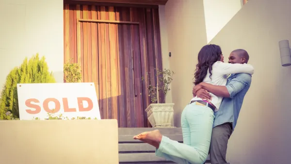 Couple embracing happily in front of home with "SOLD" sign