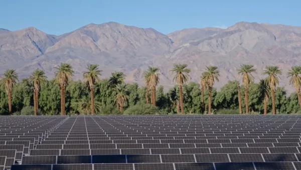 Array of solar panels in the foreground with palm trees and mountains in background, Death Valley, California