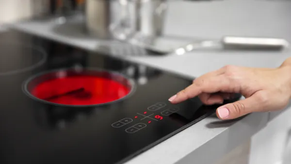 Close-up of black electric stove with red heated coil and person reaching out to press button