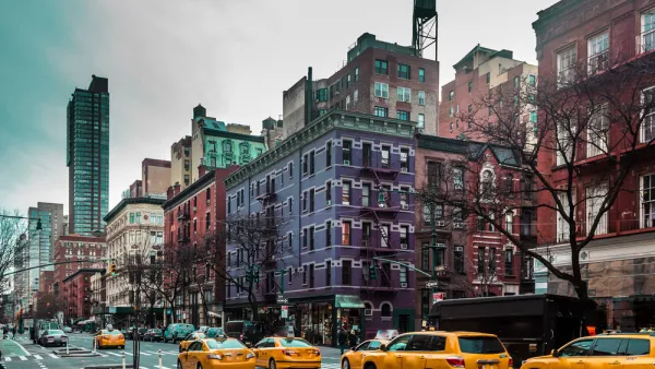 View of New York City street with yellow cabs and purple and red brick apartment buildings in background