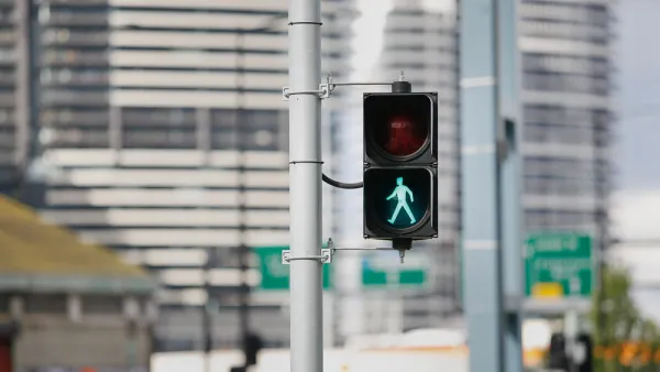 Pedestrian stoplight with green 'walk' silhouette lit up and blurry city buildings in background