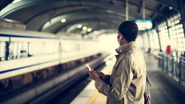 Person on subway platform holds phone and looks toward track
