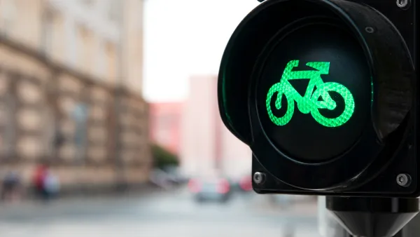 Close-up of black traffic light with green bike symbol lit up and blurry urban scene in background