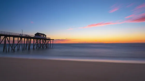View of empty beach with wooden fishing pier going out into Atlantic Ocean at sunset in New Jersey