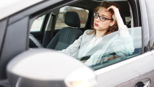 Woman in car stuck in traffic, leaning on her elbow in frustration