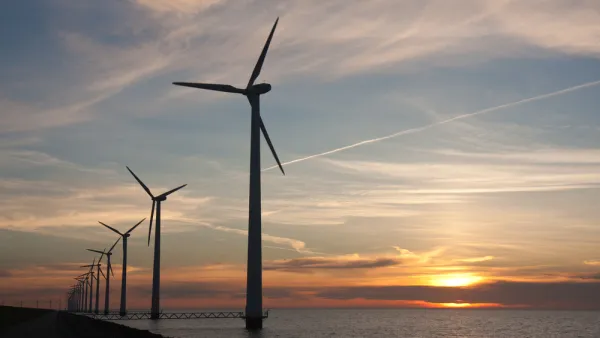 Line of offshore wind turbines with sunset over sea in the background