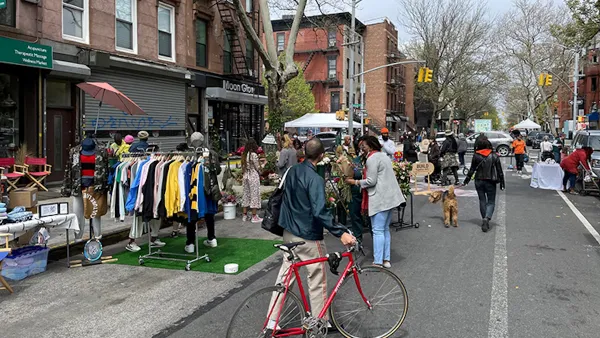 Man with red bicycle walks bike down 'open street' with vendor booths in New York City.